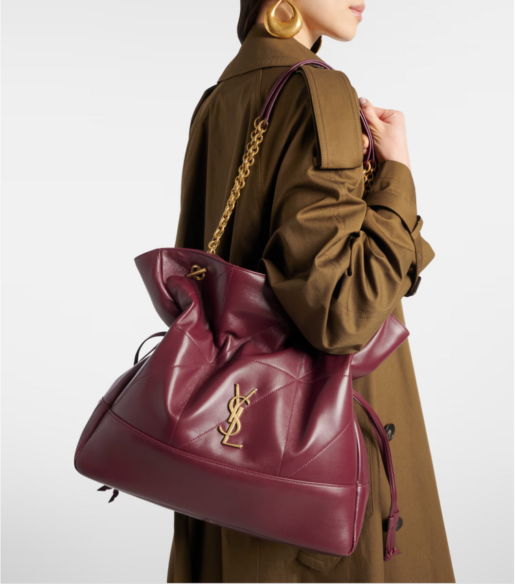 Person wearing a brown coat with a large burgundy handbag featuring a gold chain and YSL logo.