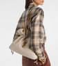 Person wearing a beige drawstring bag with a YSL logo, plaid shirt, and brown pants on a white background.