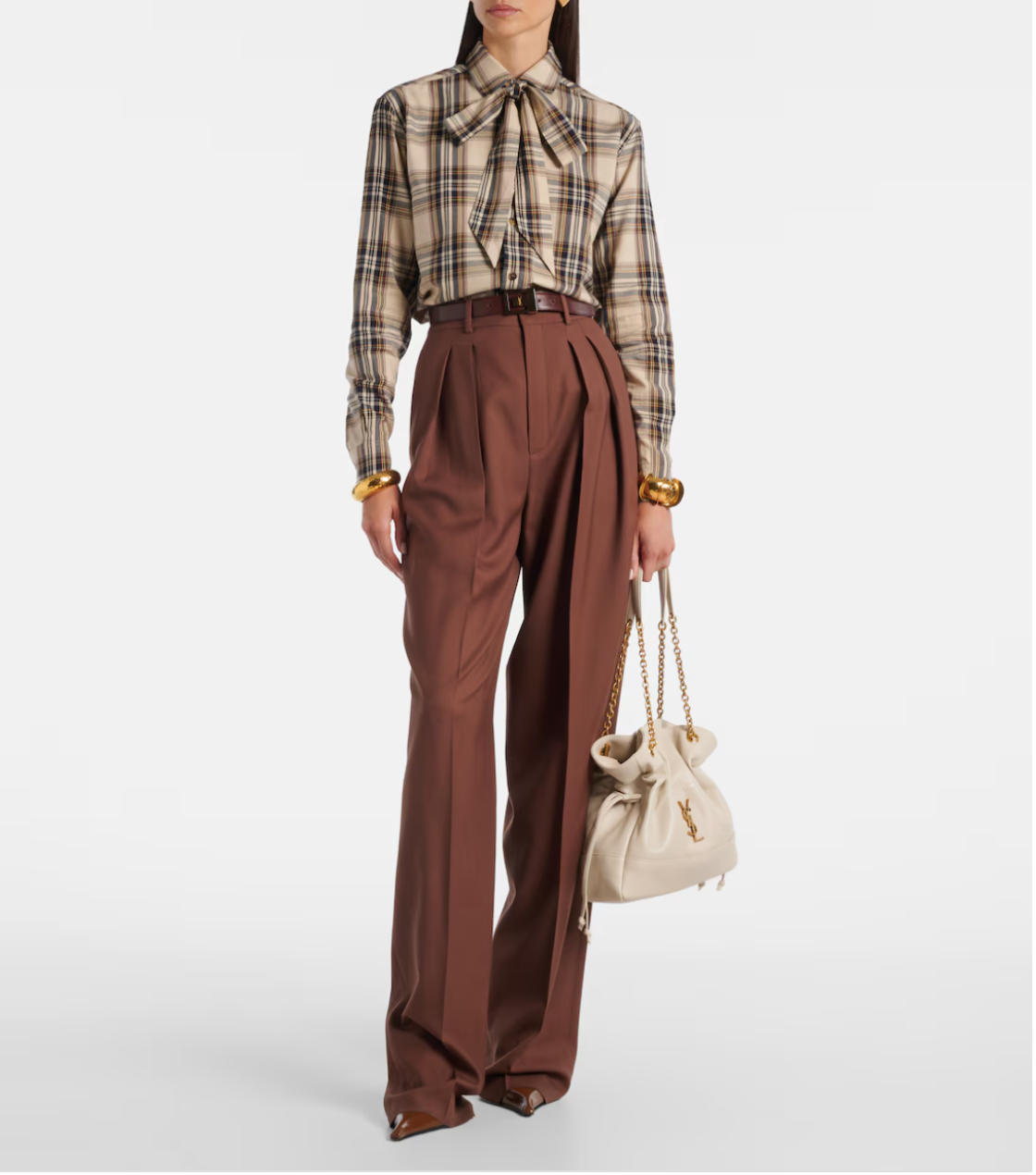 Person wearing a plaid shirt and brown pants holding a beige handbag on a white background