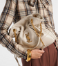 Person holding a cream-colored handbag with gold chain and YSL logo, wearing a plaid shirt and gold bracelet.