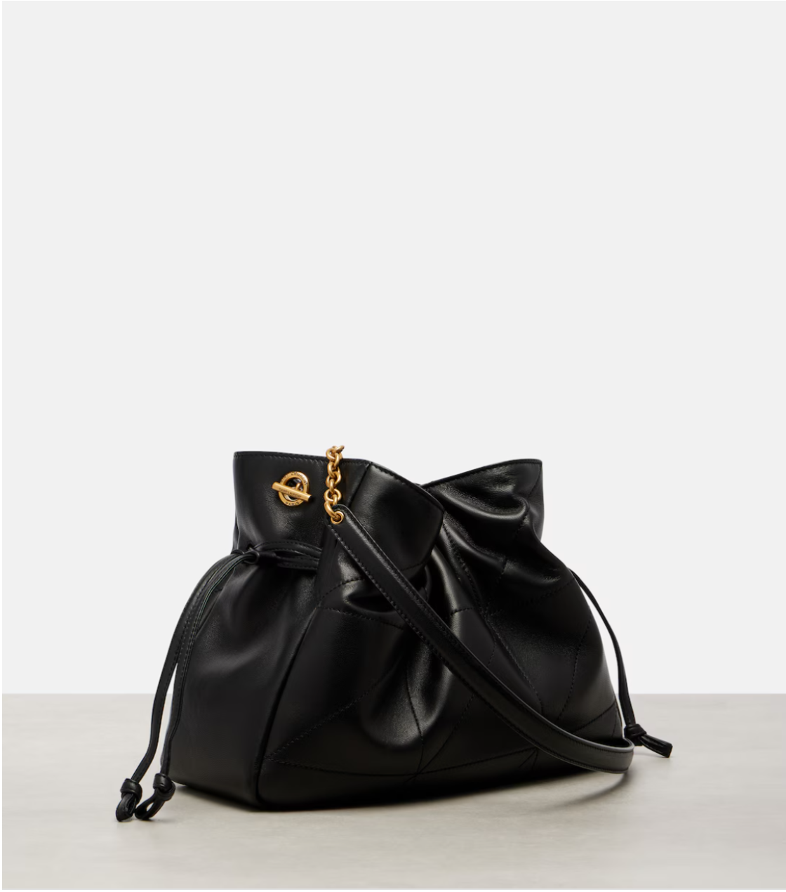 Black leather drawstring YSL bag with gold chain on a light gray background