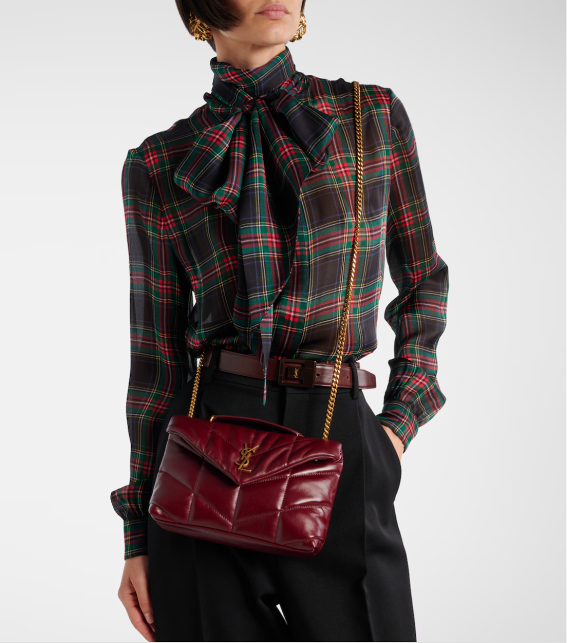 Person wearing a plaid shirt with a bow tie and holding a red handbag.