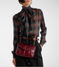 Person wearing a plaid shirt with a bow tie and holding a red handbag.