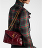 Person wearing a red plaid coat with a burgundy handbag featuring a gold chain strap.