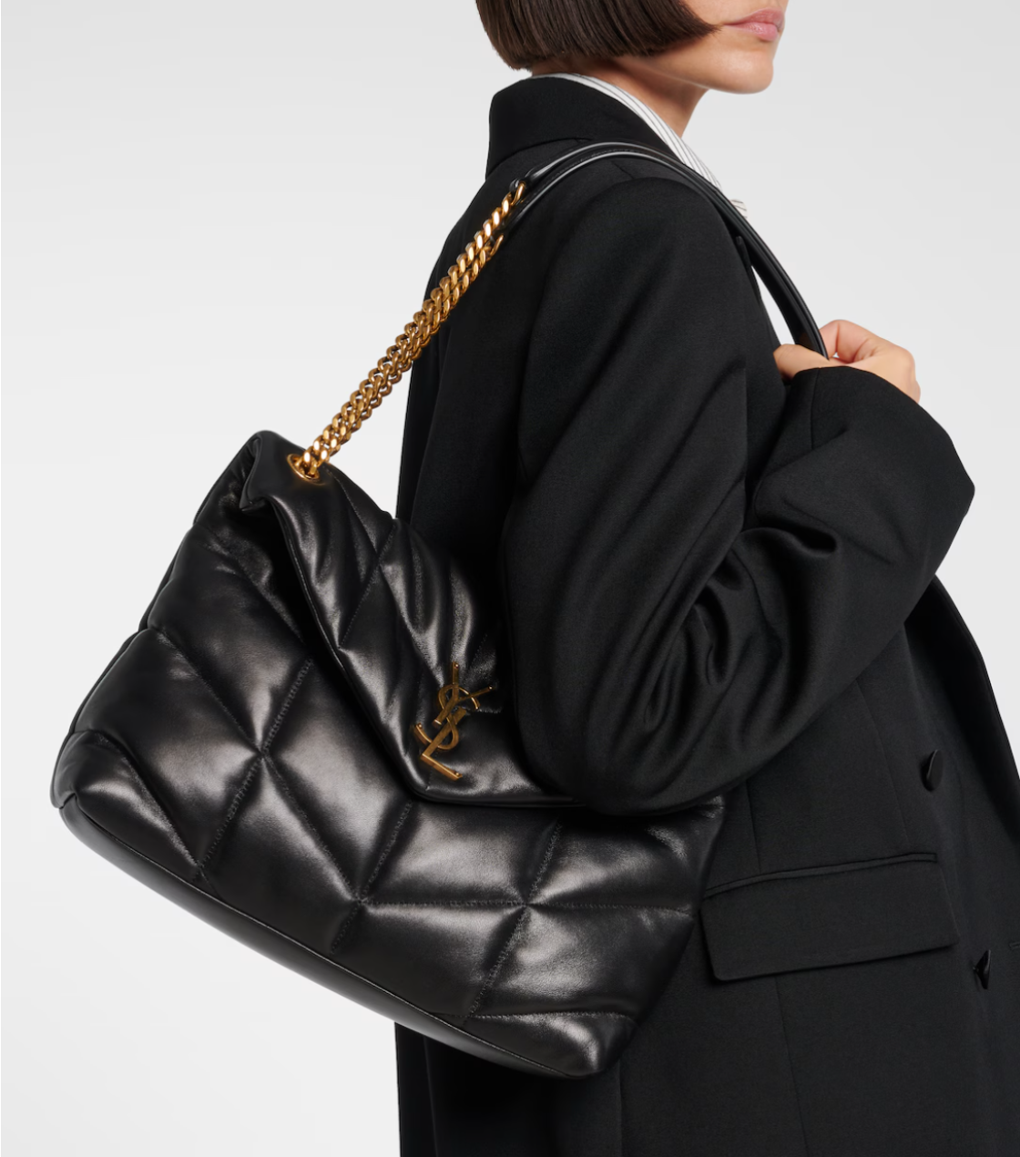 Person wearing a black quilted handbag with a gold chain strap on a light gray background