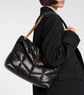 Person wearing a black quilted handbag with a gold chain strap on a light gray background