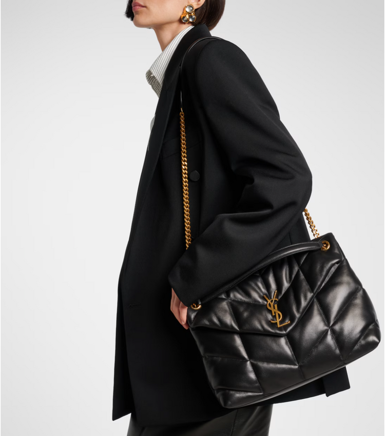 Person holding a black quilted handbag with gold chain strap on a white background
