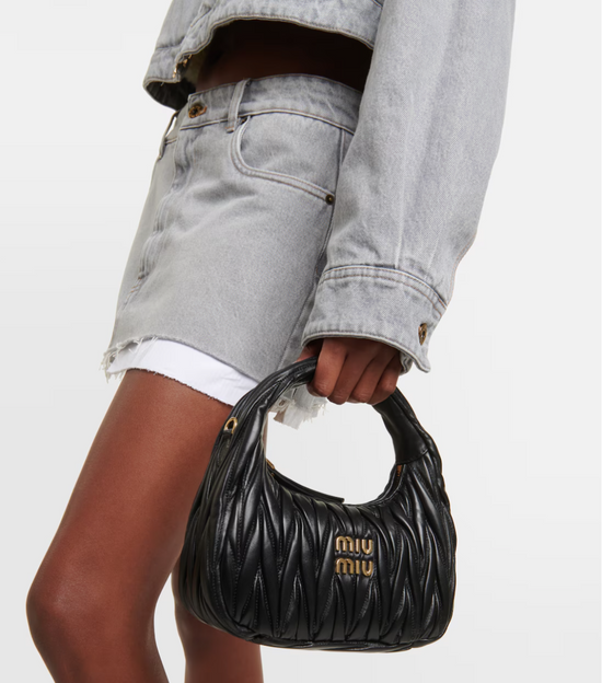 Person holding a black Miu Miu handbag against a neutral background