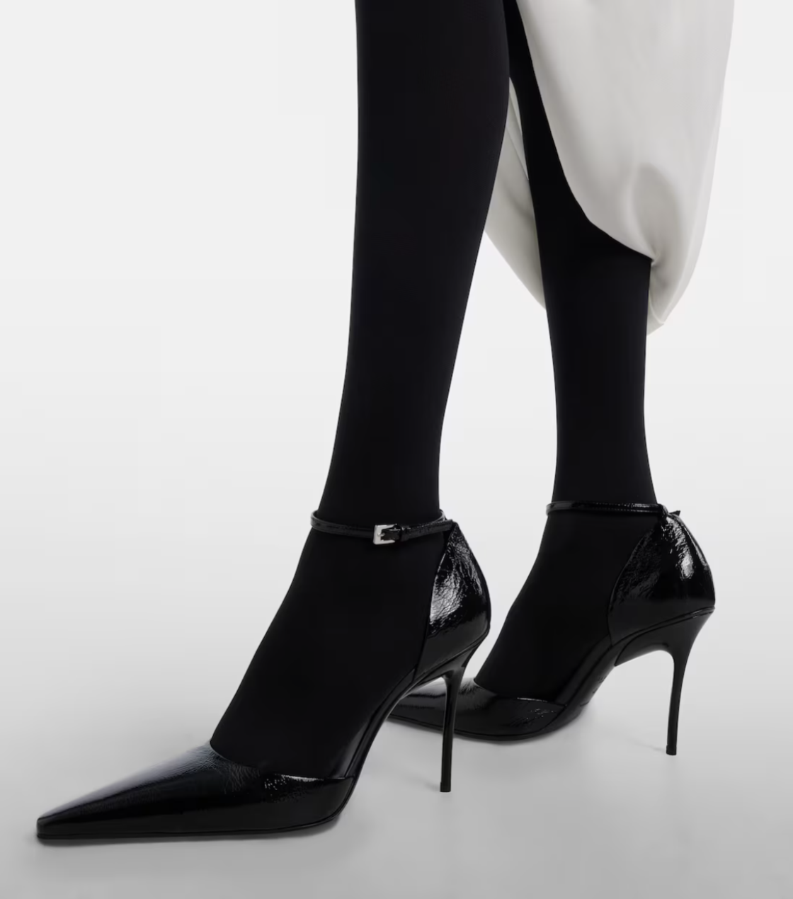 Black high-heeled shoes worn with black tights on a white background