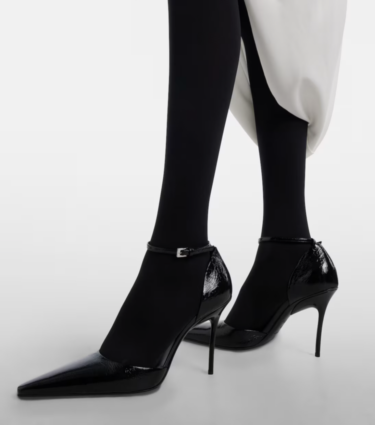 Black high-heeled shoes worn with black tights on a white background