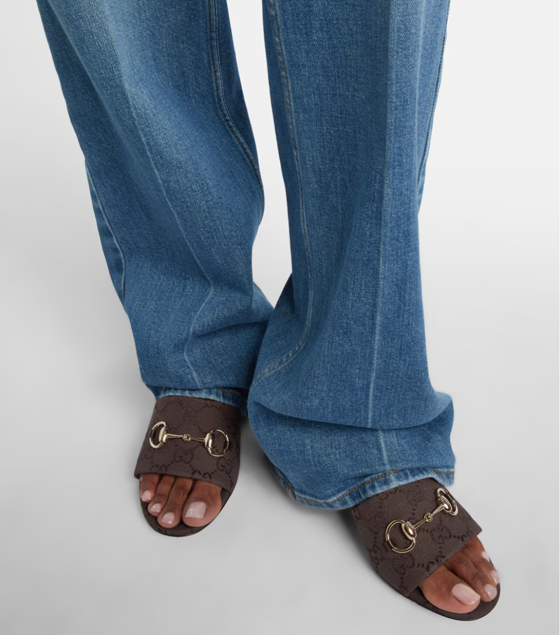 Blue jeans worn with brown sandals on a light gray background