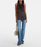 Woman wearing a brown sleeveless top with a tie detail and blue jeans, holding a beige handbag on a white background.