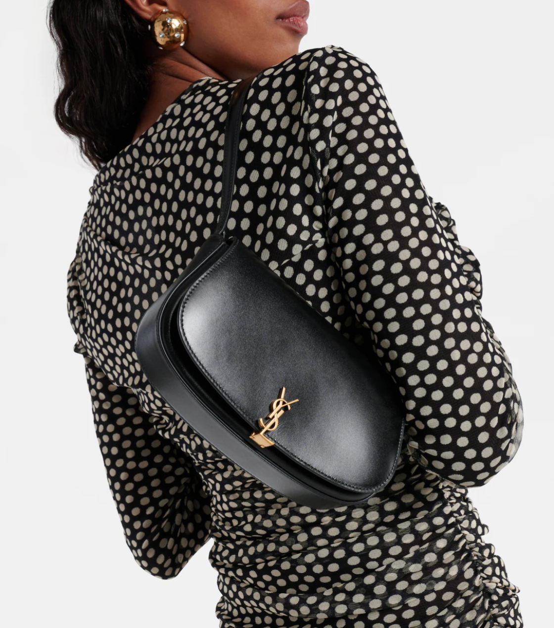 Person wearing a black polka dot dress with a black handbag featuring a gold logo.
