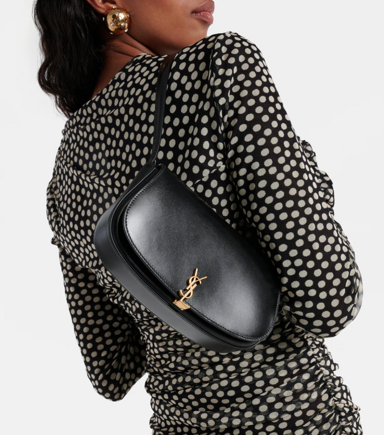 Person wearing a black polka dot dress with a black handbag featuring a gold logo.