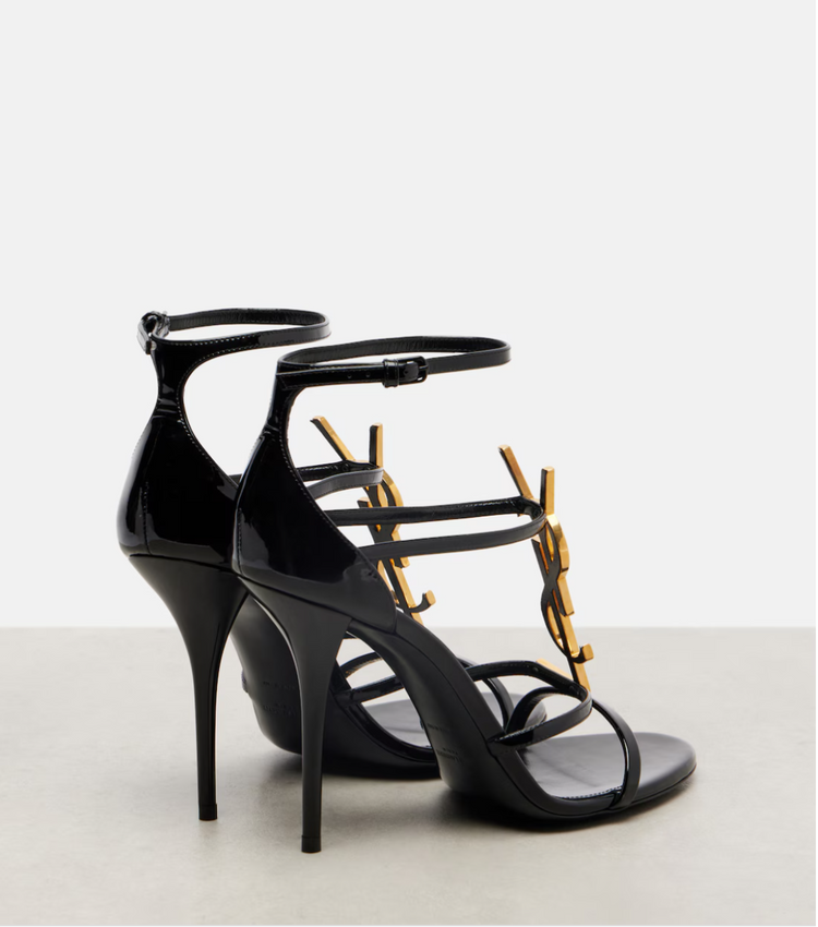 Black high-heeled sandals with gold accents on a light gray background