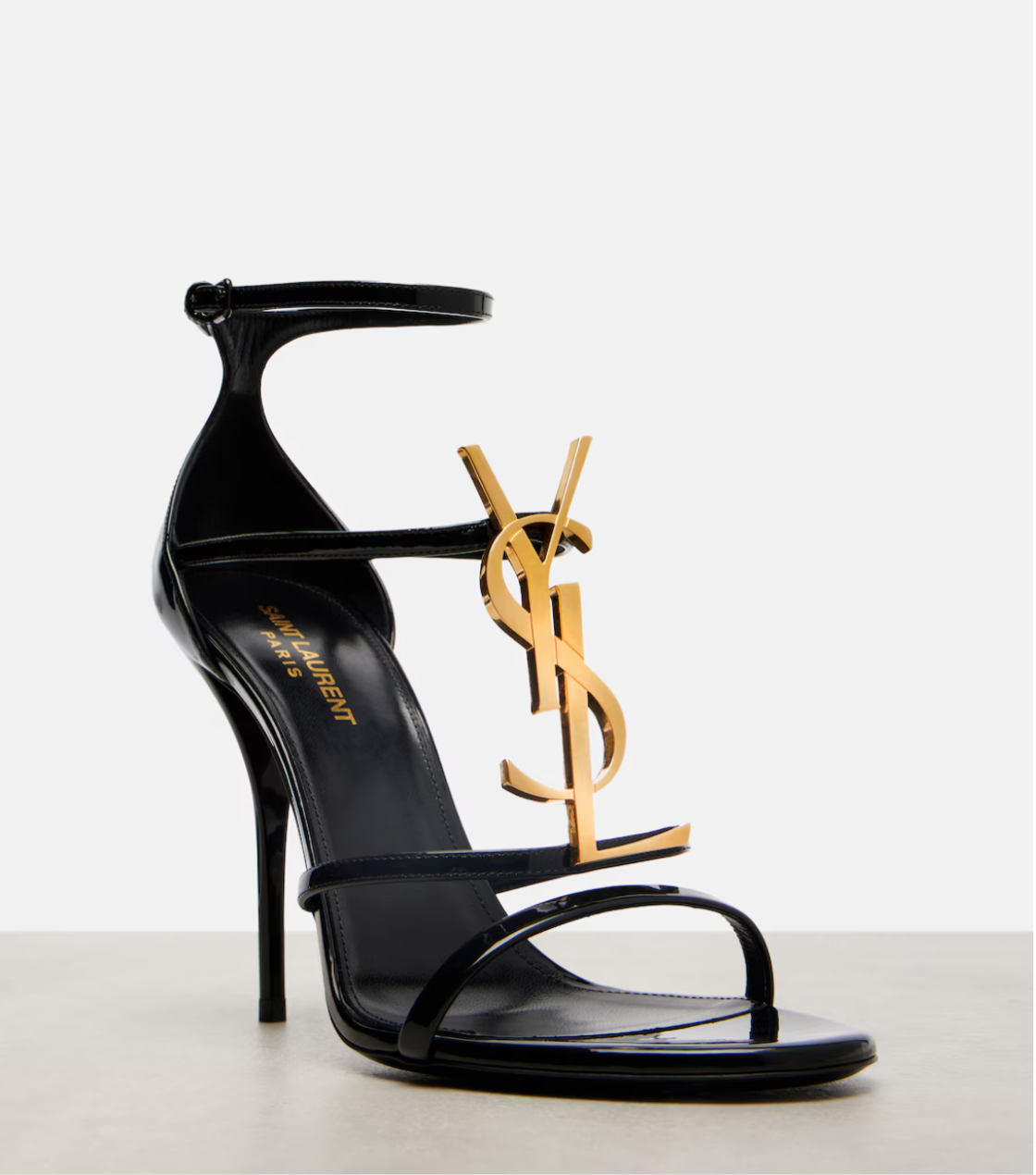 Black high-heeled sandal with gold logo on a white background