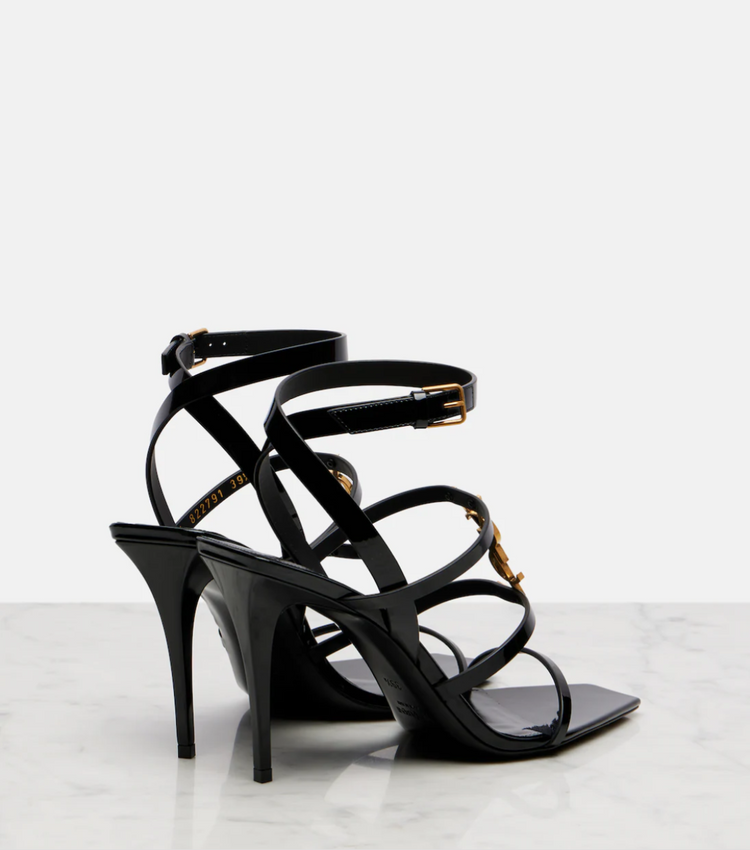 Black high-heeled sandals with strappy design on a light gray background