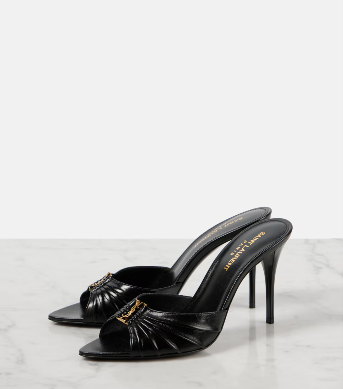 Black high-heeled shoes with gold accents on a white marble surface