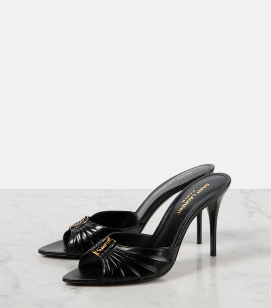 Black high-heeled shoes with gold accents on a white marble surface