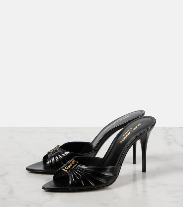 Black high-heeled shoes with gold accents on a white marble surface