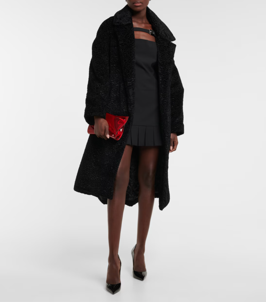 Person wearing a black coat and dress with a red clutch on a white background