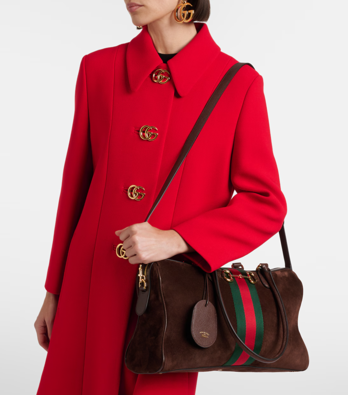 Person wearing a red coat with gold buttons holding a brown handbag with green and red stripes.