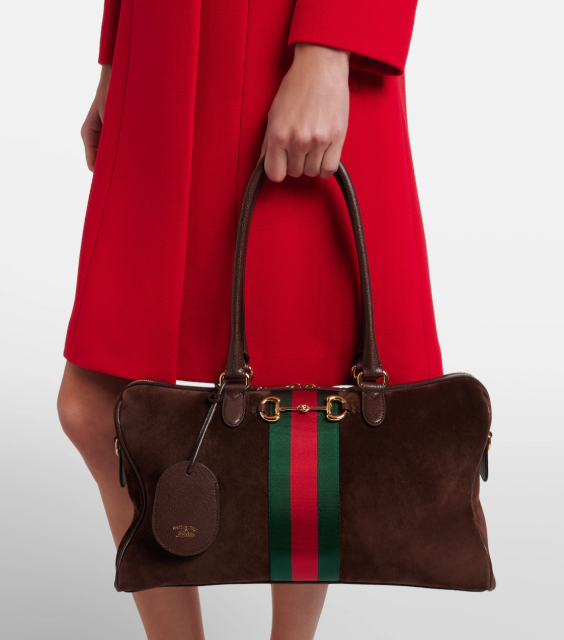 Brown handbag with red and green stripes held by a person wearing a red coat on a white background