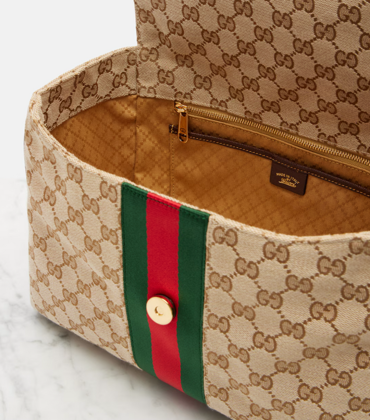 Designer handbag with monogram pattern and red and green stripe on a marble surface