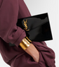Black clutch with gold accents held by a person wearing a burgundy outfit.