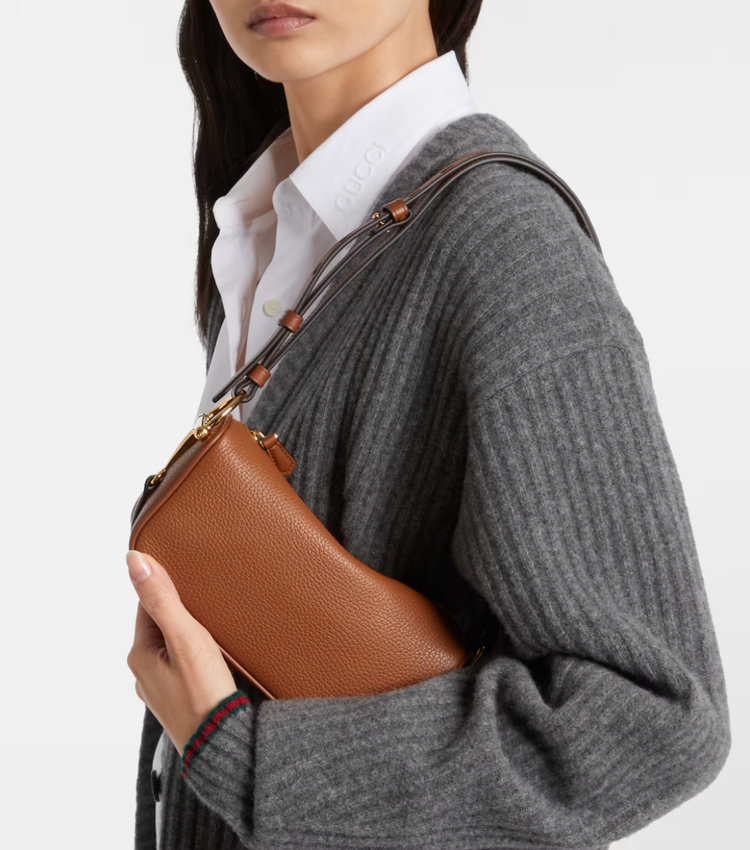 Person wearing a gray sweater holding a brown leather handbag.