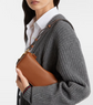 Person wearing a gray sweater holding a brown leather handbag.
