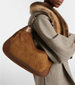 Brown textured handbag held by a person wearing a gray coat with fur collar.