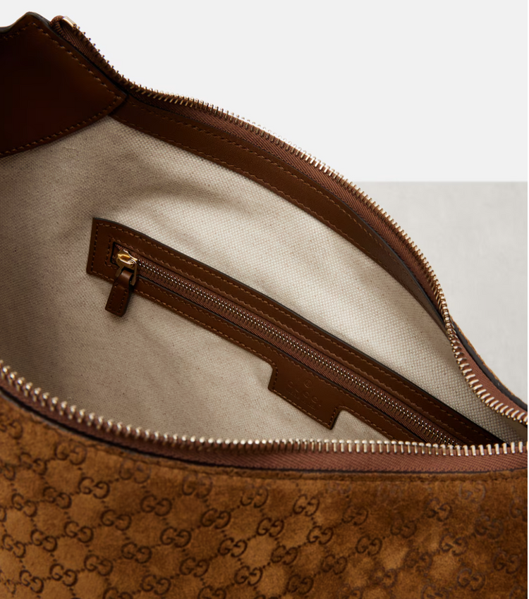 Close-up of a brown leather bag with a zipper, featuring the Gucci logo.