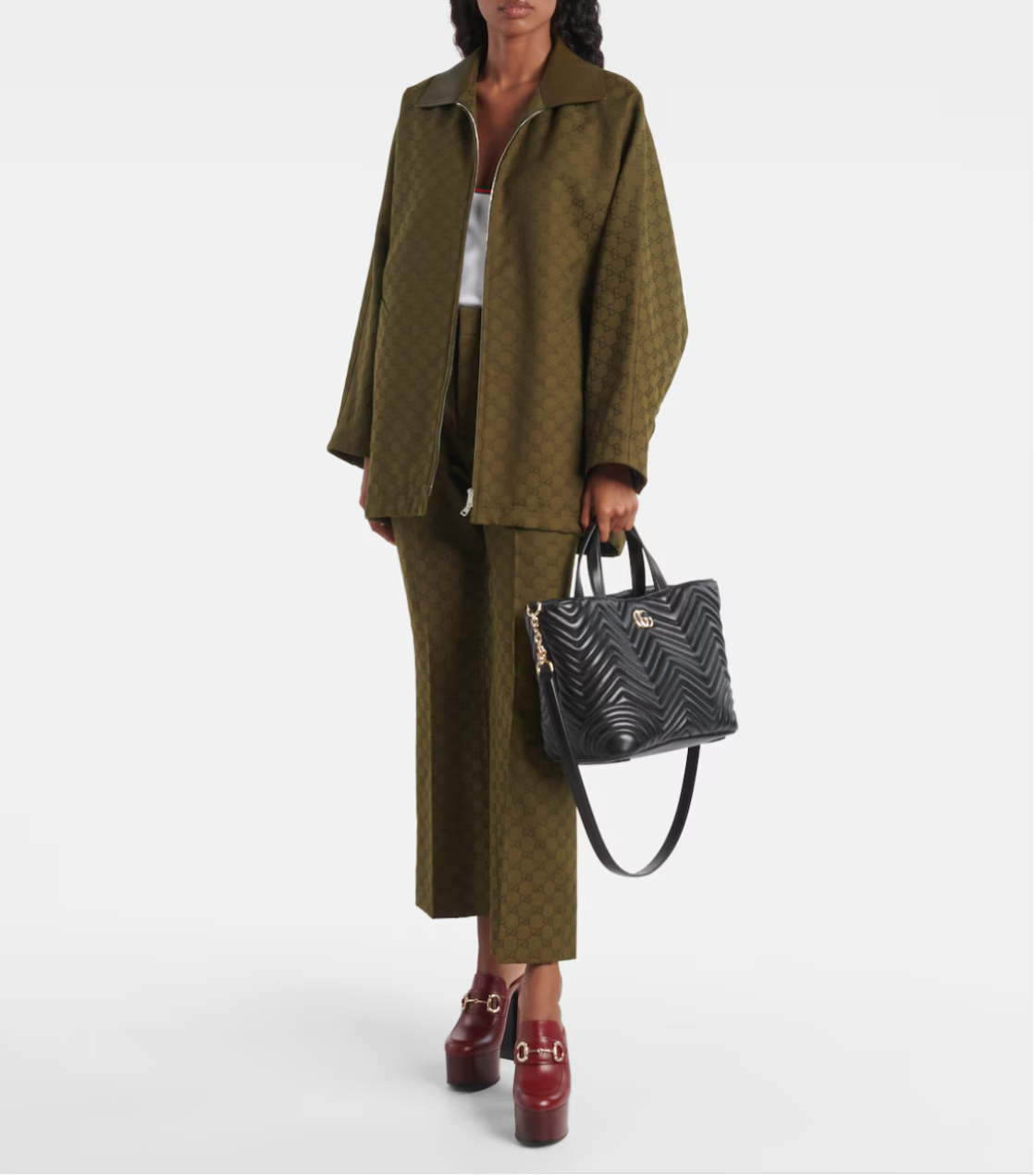 Person wearing a green textured outfit with a black handbag on a white background