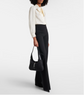 Person wearing a white blouse and black pants holding a black handbag on a white background