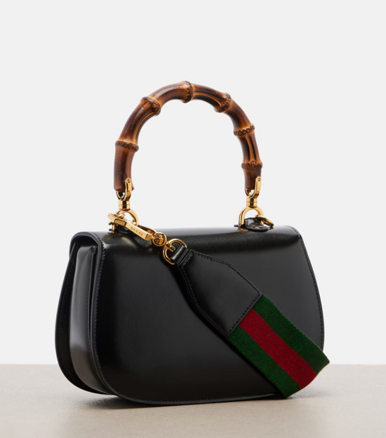 Black handbag with bamboo handle and iconic green and red stripe on a light gray background