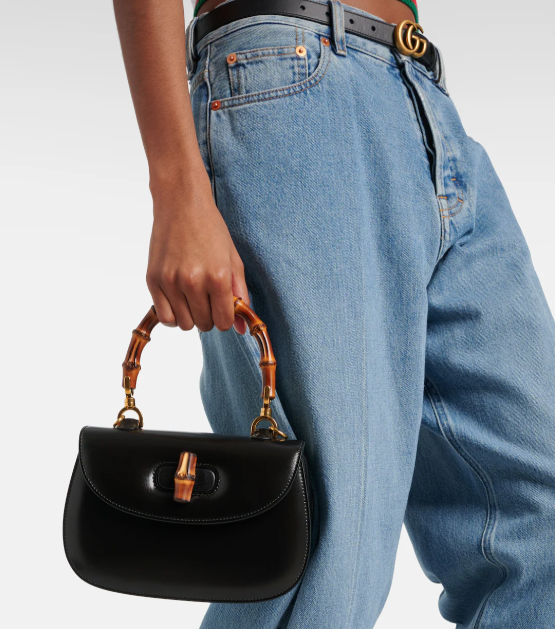 Person holding a black handbag with wooden handle and Gucci belt in the background