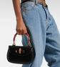 Person holding a black handbag with wooden handle and Gucci belt in the background