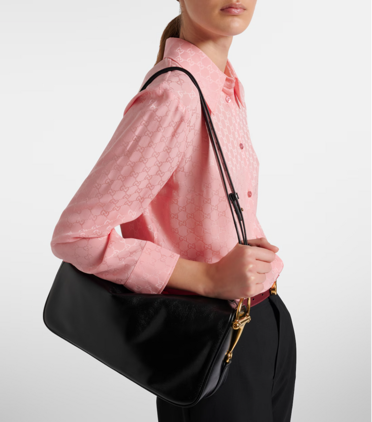 Person wearing a pink shirt and holding a black handbag with a gold zipper.