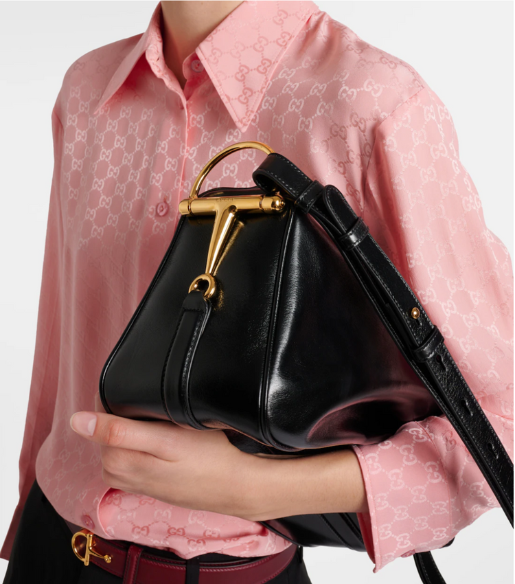 Person holding a black handbag with gold accents against a pink shirt background