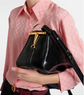 Person holding a black handbag with gold accents against a pink shirt background