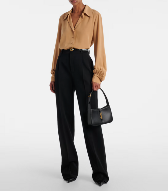 Person wearing a beige shirt and black pants holding a black handbag on a white background