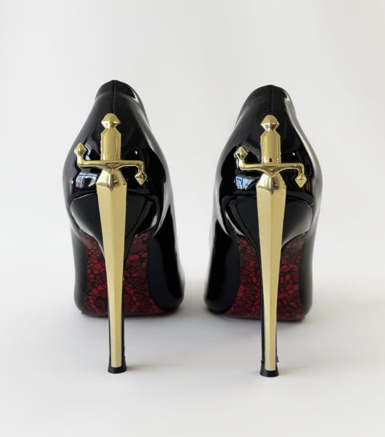 Black high-heeled shoes with gold sword designs on a white background